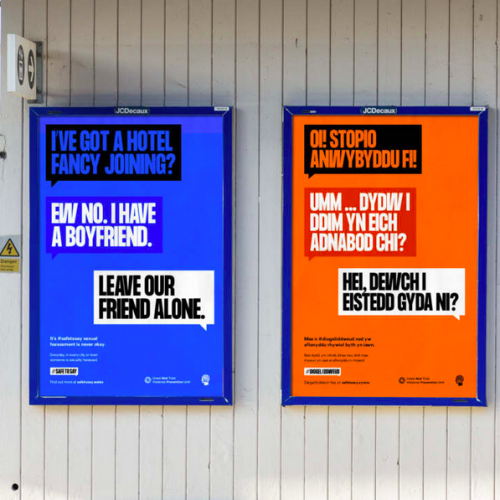 Two adjacent posters, one English language and one Welsh language, at a train station in Cardiff. Both posters depict a conversation via speech bubbles. The English language one has the first person saying 'I've got a hotel fancy joining?' to which the second person replies 'Ew no. I have a boyfriend'. A third person then interjects 'Leave our friend alone.'